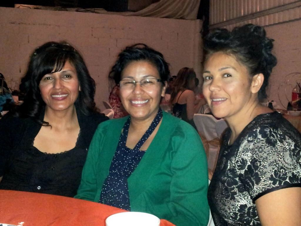 Three women smiling at an indoor event, seated at a table with a red tablecloth