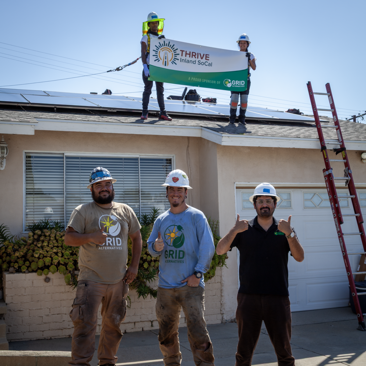 THRIVE Inland SoCal workers holding banner on residential roof with solar panels and GRID Alternatives logo