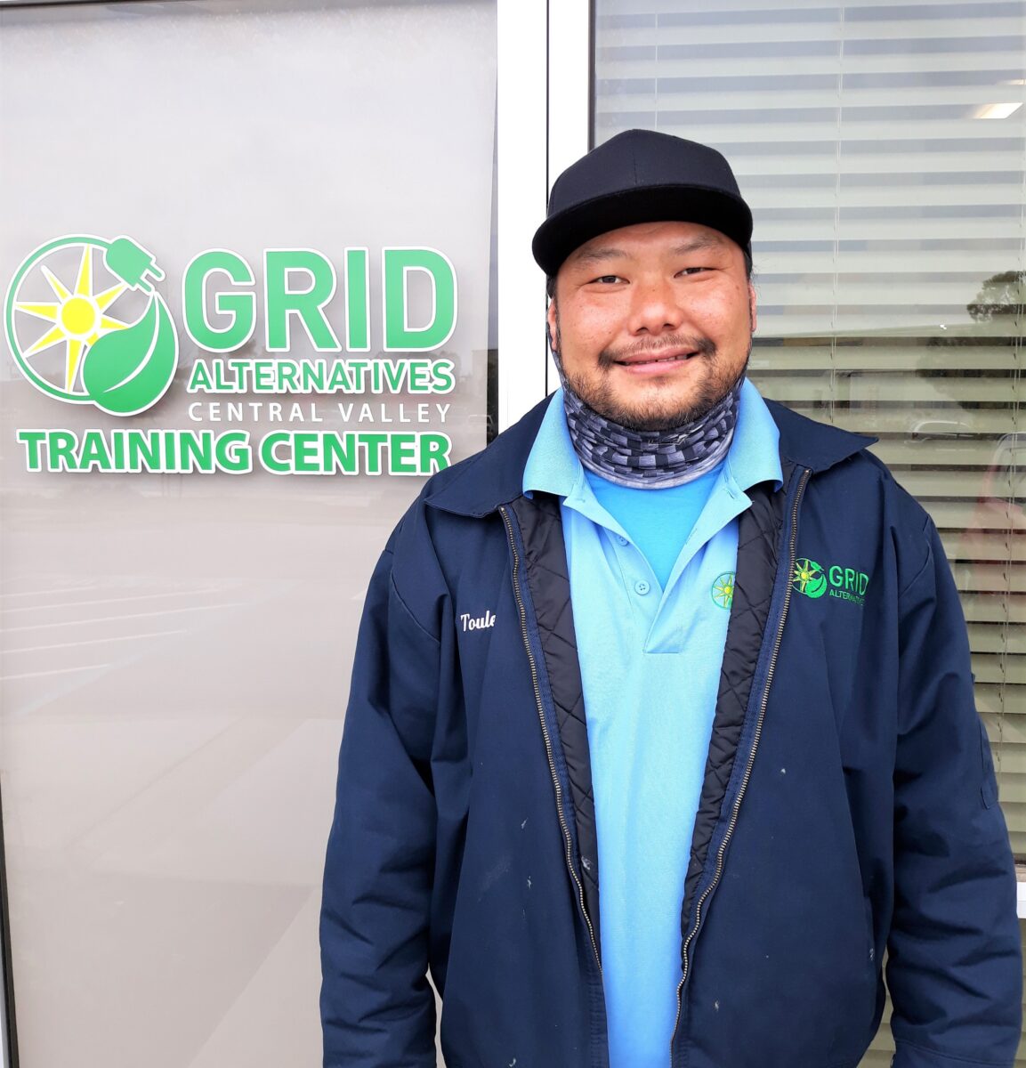 Toulee Vang smiling in front of Grid Alternatives Central Valley Training Center sign