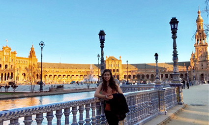Woman posing at Plaza de España in Seville with ornate yellow buildings and decorative bridge railing
