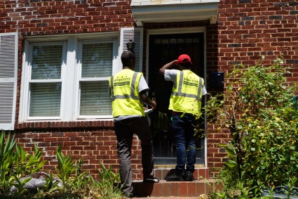 Two workers in yellow safety vests canvassing at a brick house doorway
