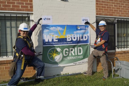 We Build volunteers, mother and daughter, pose by a We Build banner