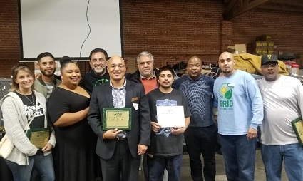 Group of volunteers holding certificates and awards in a brick warehouse, smiling at camera during appreciation event