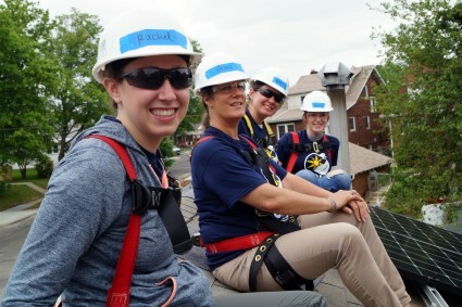Four volunteers pose on the roof of the home while installing solar