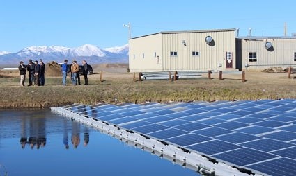 Floating solar panels on water with group touring modern building and snowy mountains beyond