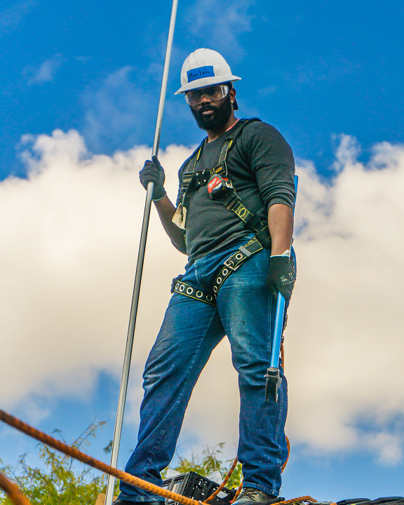 Construction worker in safety gear holding a pole against blue sky