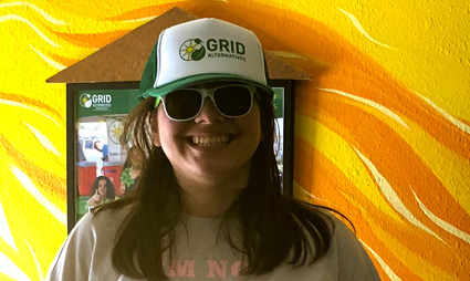 Person wearing GRID cap and sunglasses smiling in front of yellow abstract background