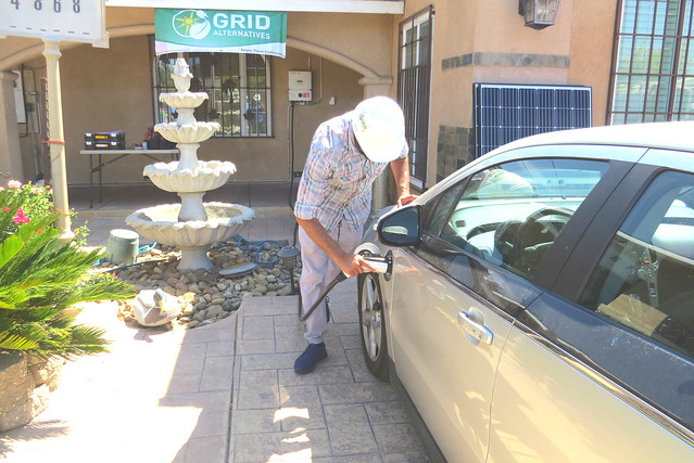 Man charging electric vehicle outside Grid Alternatives storefront