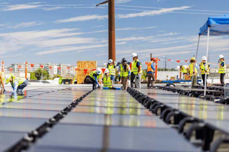 A large crew in safety vests works across a flat commercial roof covered in panels.