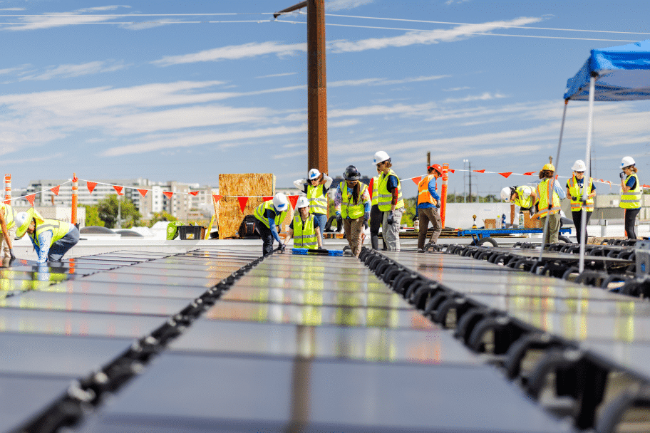 A large crew in safety vests works across a flat commercial roof covered in panels.