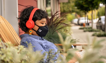 Person wearing red headphones and black face mask outdoors on a sunny day