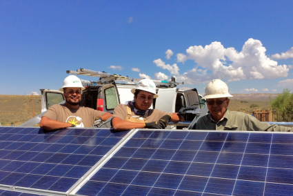 Sergeant Alvin Harvey, Steven Bitah & John Bitah smile behind a solar panel