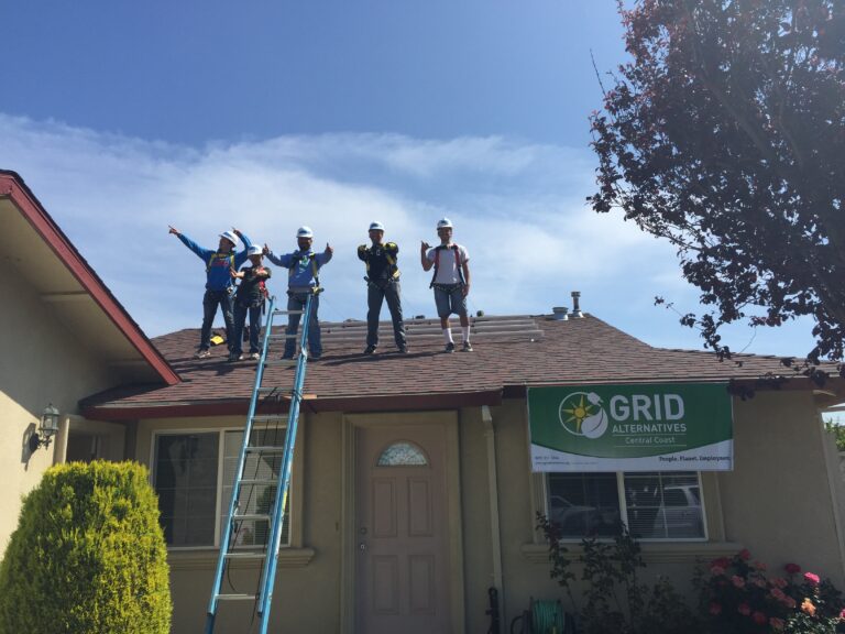 Five workers on a house roof with ladder and safety gear, GRID Alternatives Central Coast banner visible