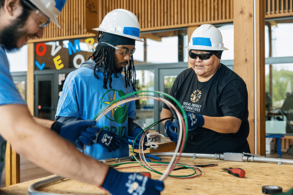 Three workers in hard hats examine electrical wiring and cables during a training program
