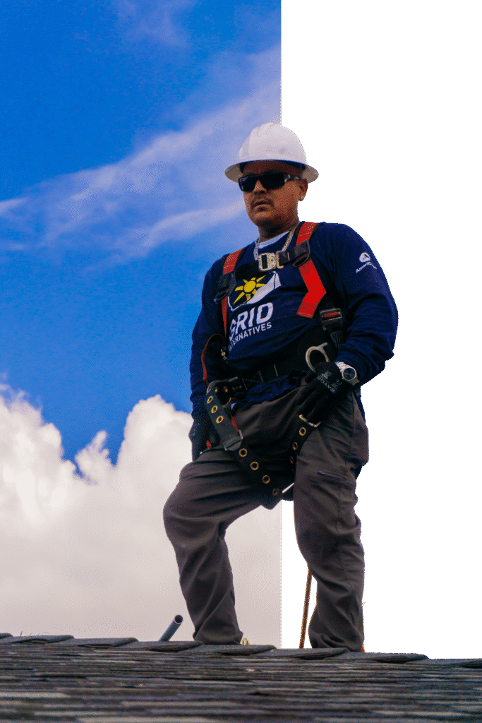 Worker in safety harness and hard hat on roofing structure against blue sky
