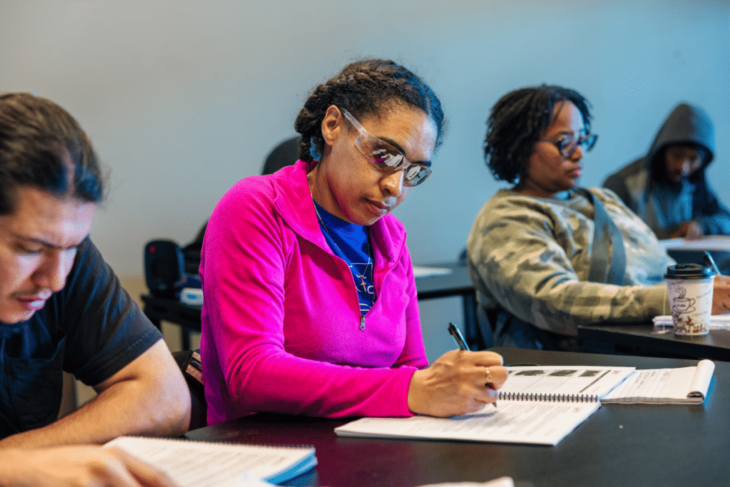 Students in a classroom taking notes during an educational session on a blue wall background