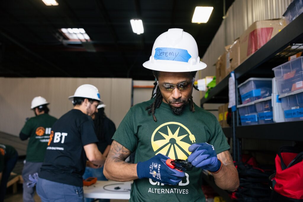 A trainee in a GRID T-shirt, hard hat and work gloves during a hands-on workshop session.