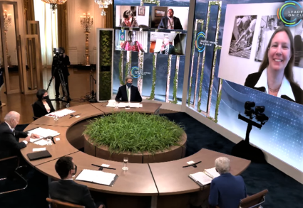 Hybrid meeting with participants seated at curved table and multiple video conference screens displaying remote attendees
