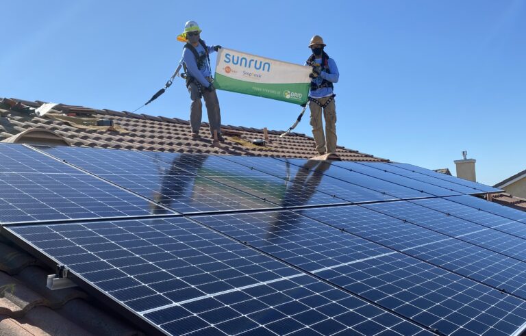 Two workers on a residential roof with solar panels, holding a Sunrun banner during installation