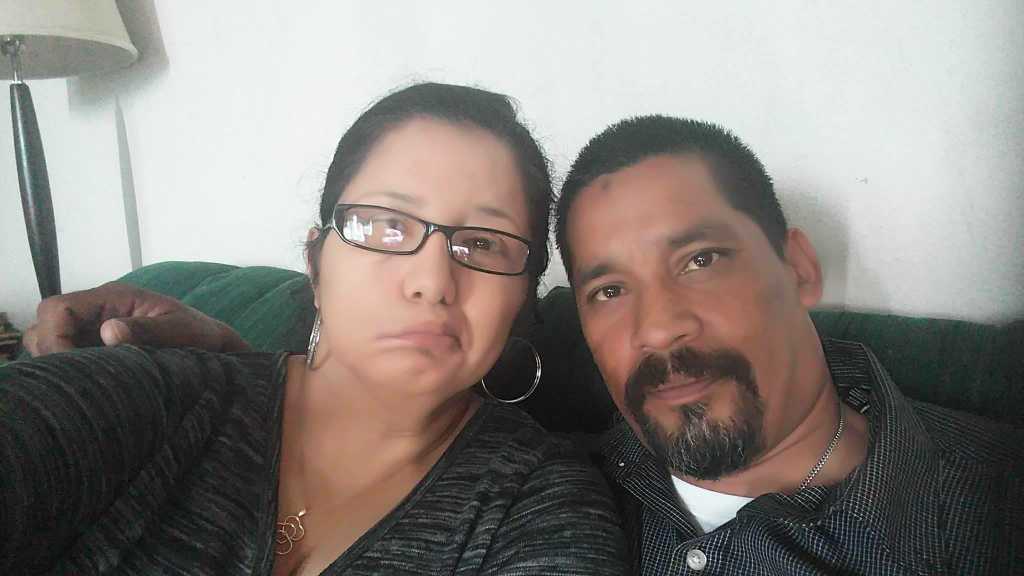 Two people sitting on a green couch taking a selfie together indoors