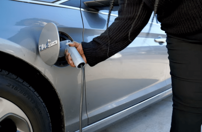 A close-up of a hand plugging a charging connector into an electric vehicle's charge port.