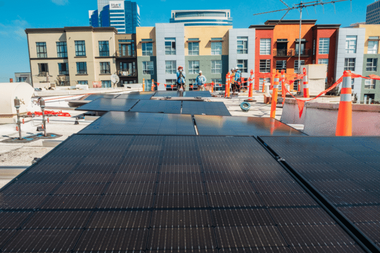 Rows of solar panels covering the flat roofs of a colorful multi-unit housing complex.