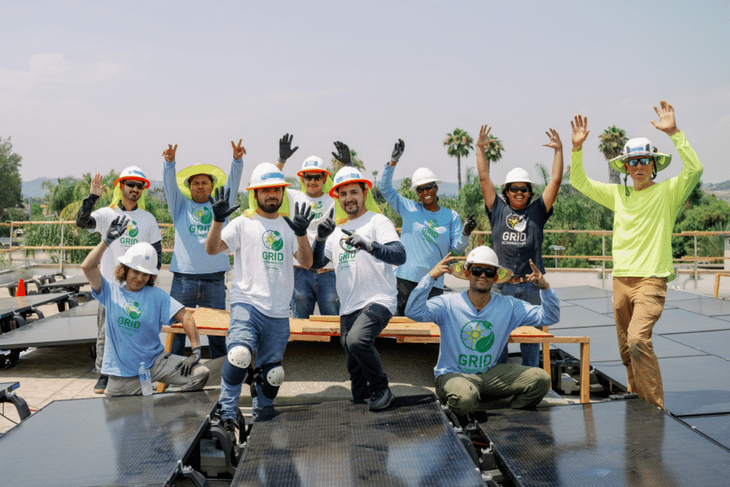 A group of installers cheers together on a rooftop lined with solar panels.
