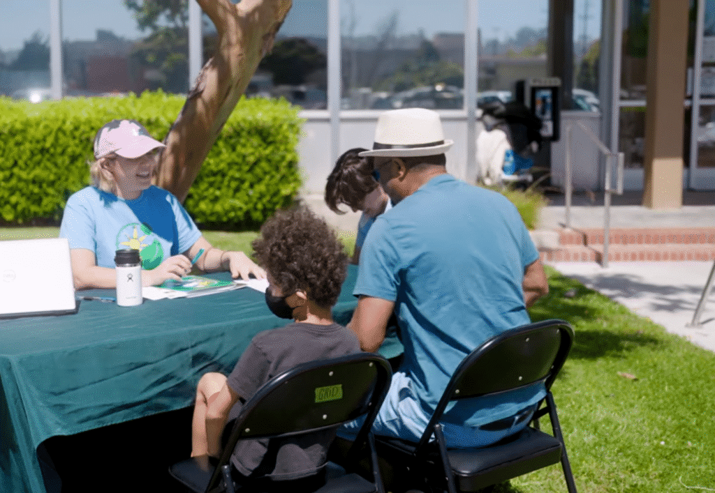 Two GRID staff members help a family fill out paperwork at an outdoor outreach table.