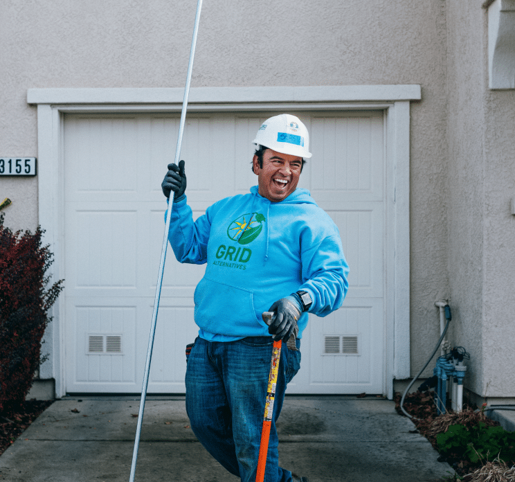 A man in a GRID hoodie stands beside solar equipment staged for a residential install.