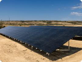 A large ground-mounted solar array on raised racking, set in an open field.