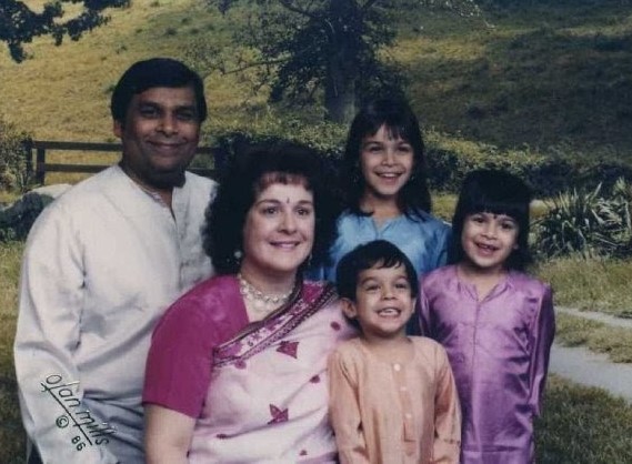 Family of five posing together outdoors with green hillside background