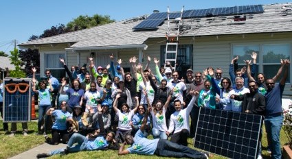 Large group of people posing in front of house with solar panels on roof