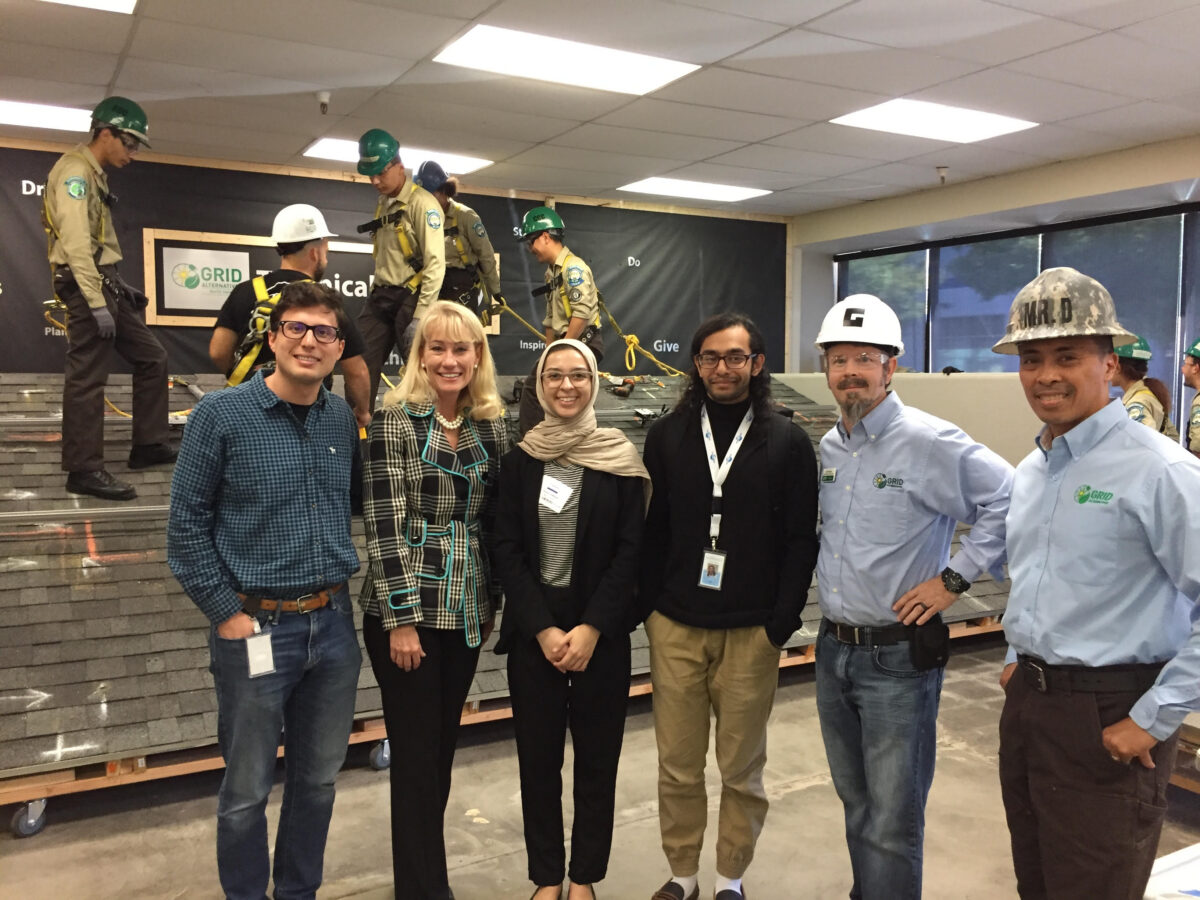 Six people posing at a GRID construction safety training event with instructors demonstrating techniques on an elevated platform behind them