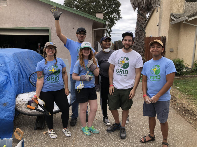 Five volunteers in GRID Alternatives t-shirts pose together at a community paint project
