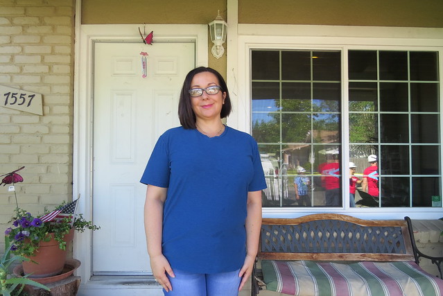 Woman in blue shirt standing on home porch with number 1557