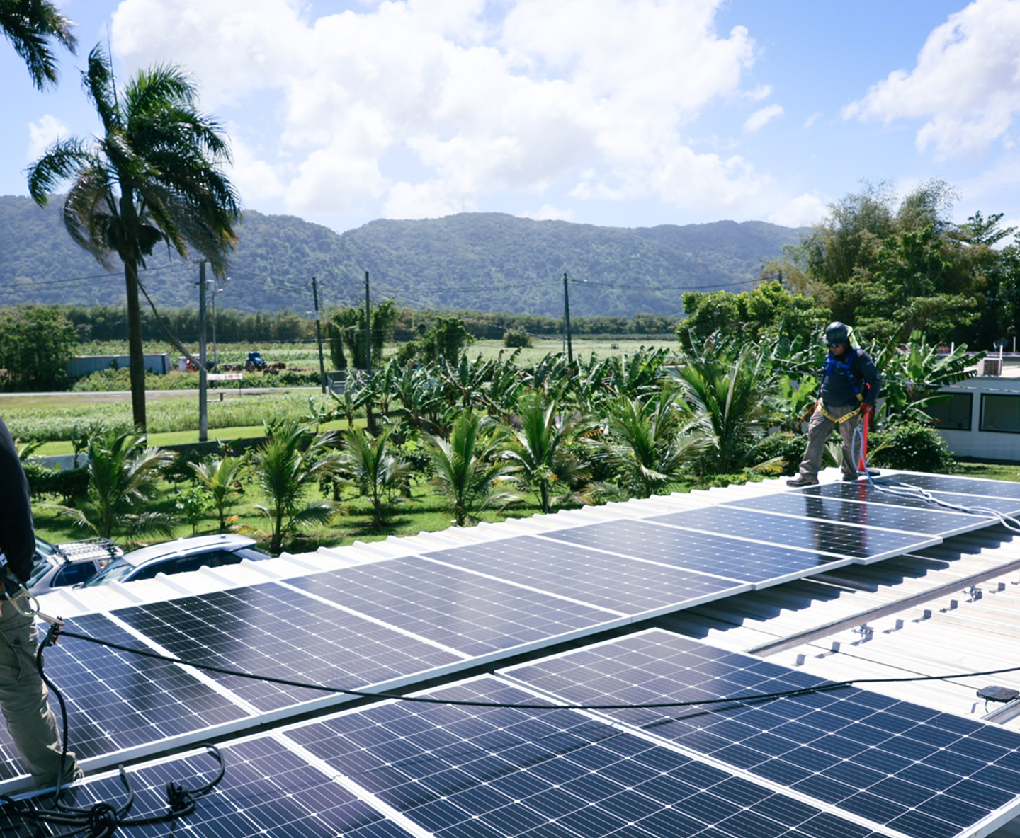 Solar panels on a rooftop with tropical agricultural fields and mountains in the background
