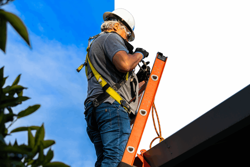 Construction worker on ladder holding level against blue sky