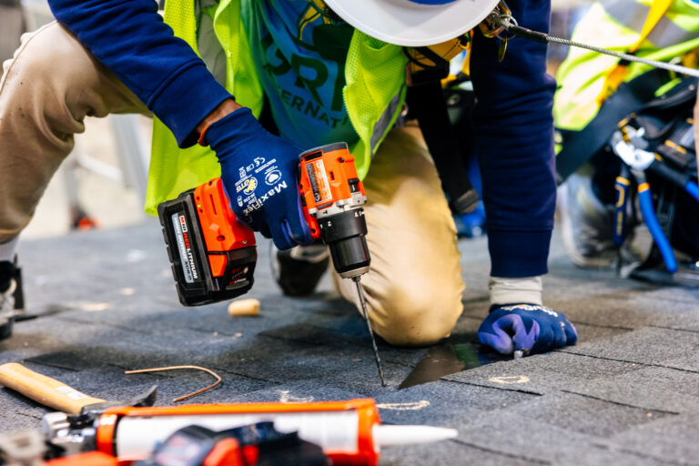 Construction worker in safety gear using cordless drill on roofing material during training
