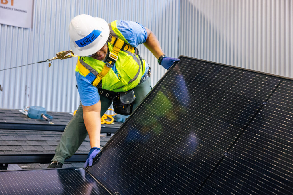 Worker in safety gear installing a solar panel on a rooftop