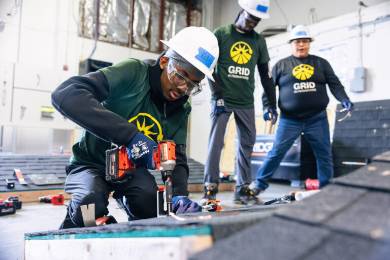 Worker using power drill during GRID training session with colleagues observing in warehouse