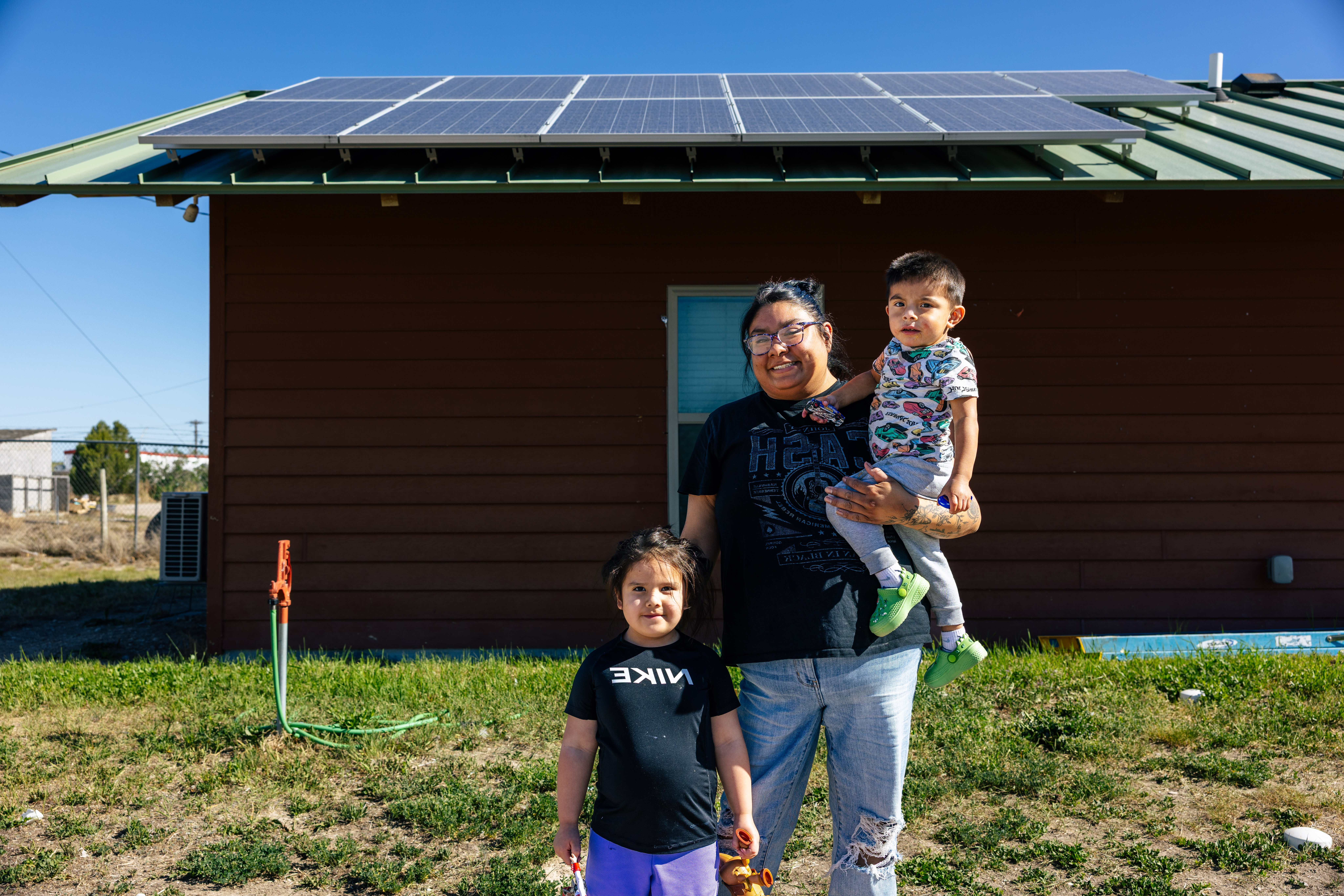 Mother holding two kids in front of home with rooftop solar