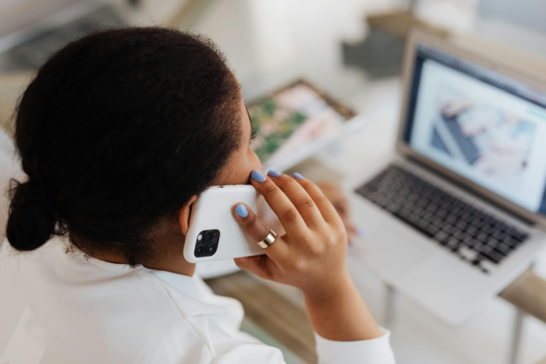 Person holding smartphone at desk with laptop, taking a call or video chat