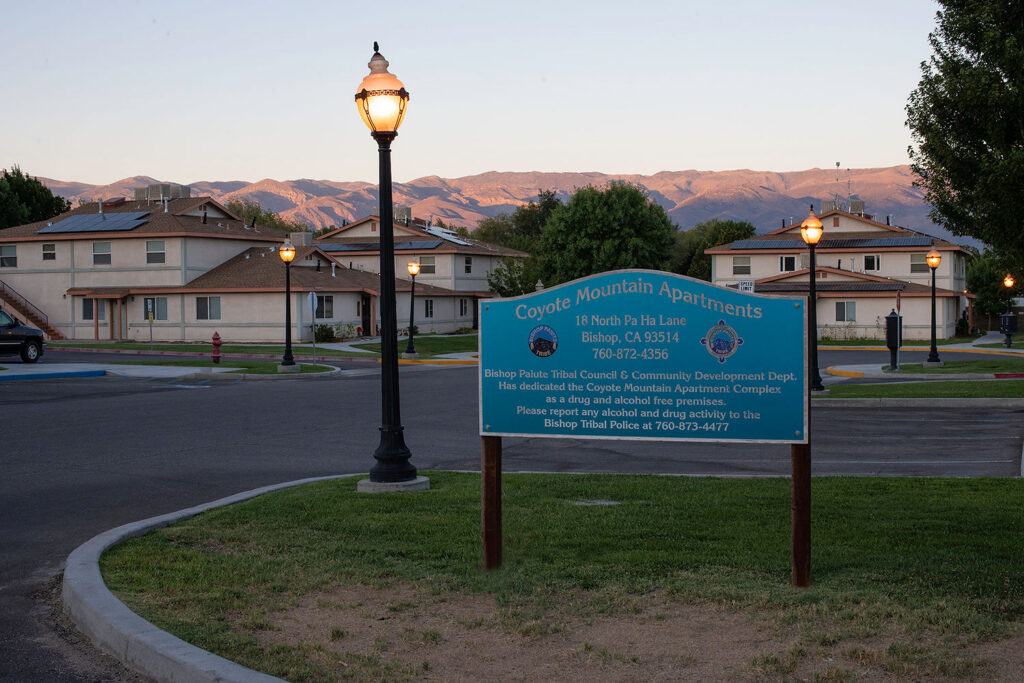 Coyote Mountain Apartments sign with street lamp and residential buildings in Bishop, California, with mountains in background