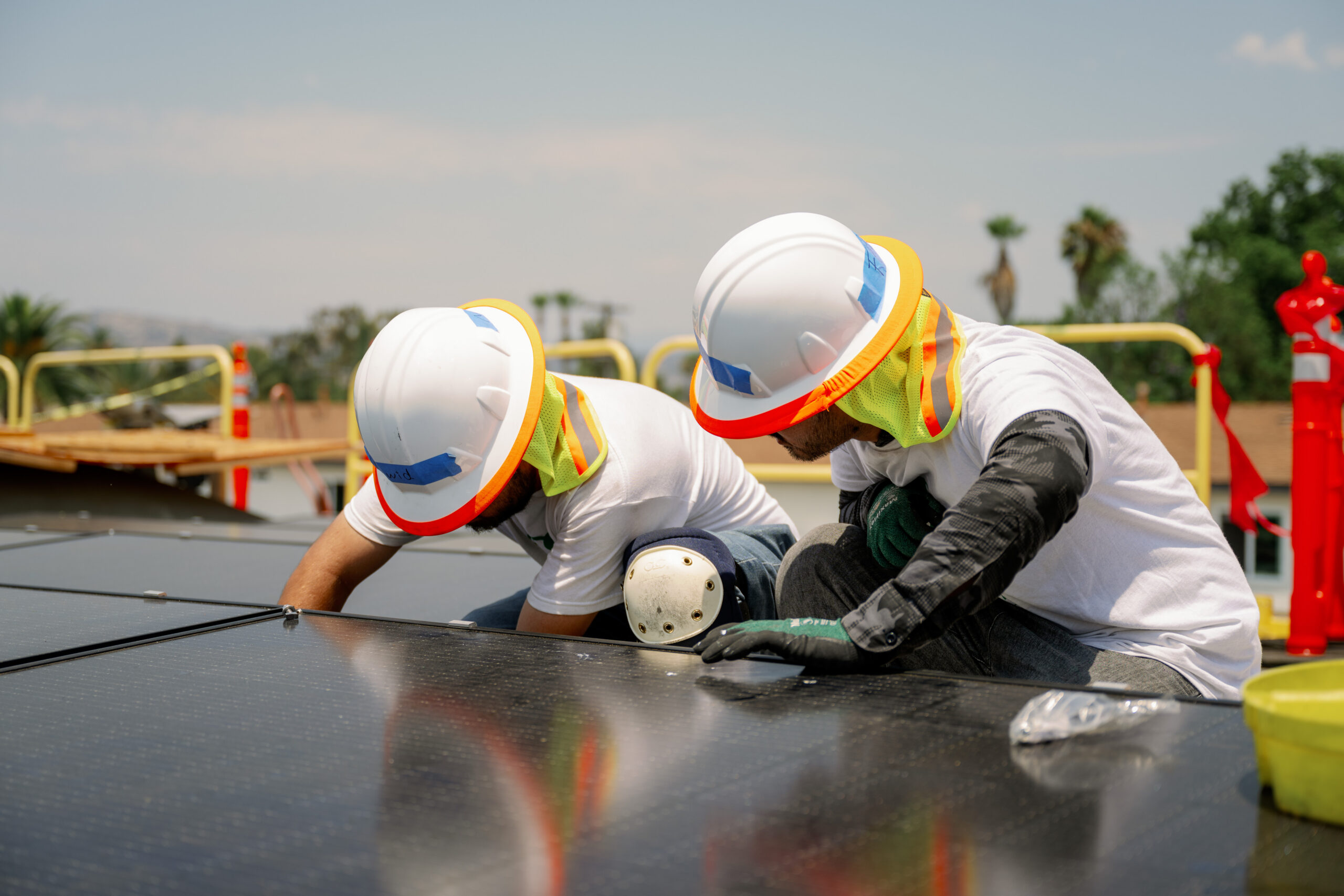 Two workers in hard hats and safety vests installing solar panels on a roof