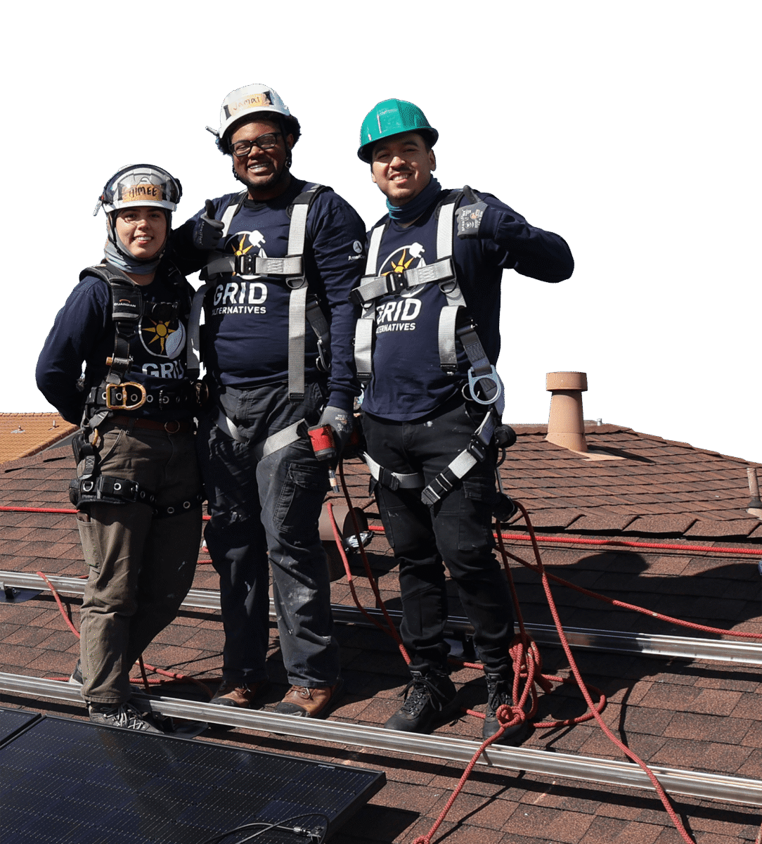 Three GRID Alternatives workers in safety gear pose on a residential roof with solar panels