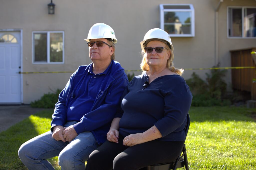 Two homeowner clients sitting in front of their home, wearing hard hats