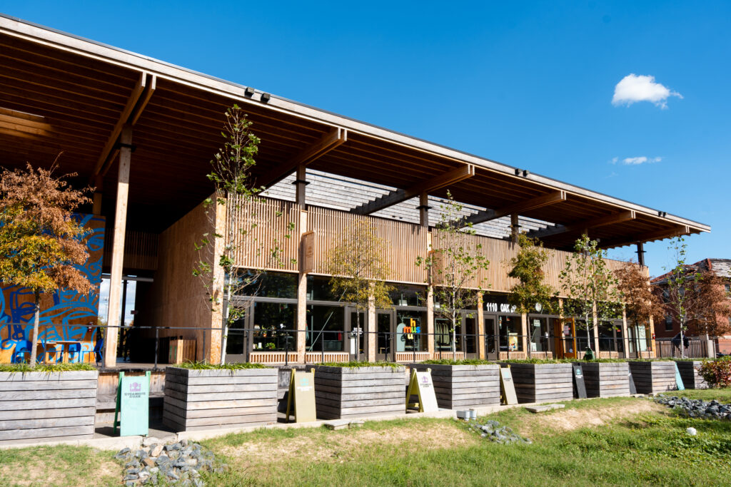 Modern wooden building with covered porch, glass storefront, and landscaped grounds on sunny day