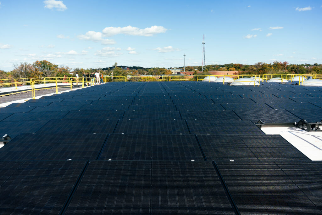 Large rooftop solar panel array with yellow safety railings and suburban landscape in background