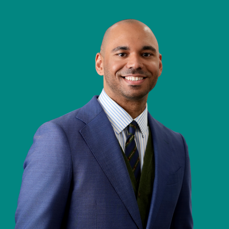 Christopher Walker, professional headshot against teal background, wearing navy blazer and striped shirt with dark tie, smiling at camera