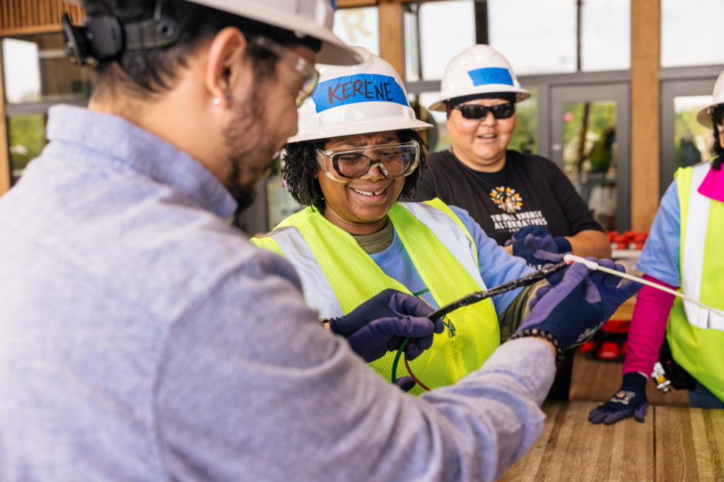 Two IBT trainees in hard hats and safety vests work together on a rooftop solar array
